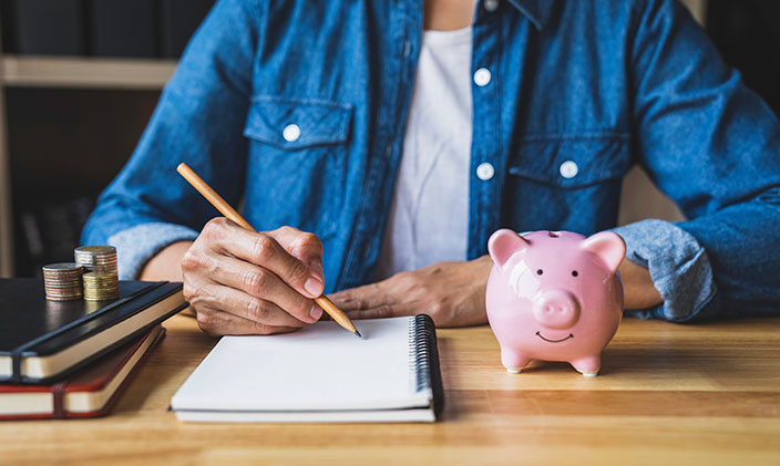 Woman writing in notebook with a piggybank on her desk